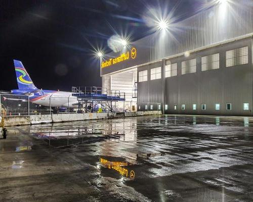 汉莎航空技术公司重型维修设施外的夜晚. Airplane entering hangar in the back.